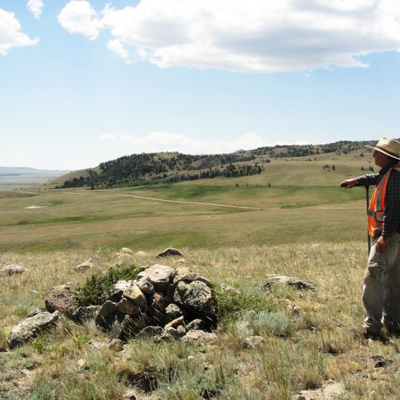 Crewmember standing next to rockpile feature with rolling landscape in background.