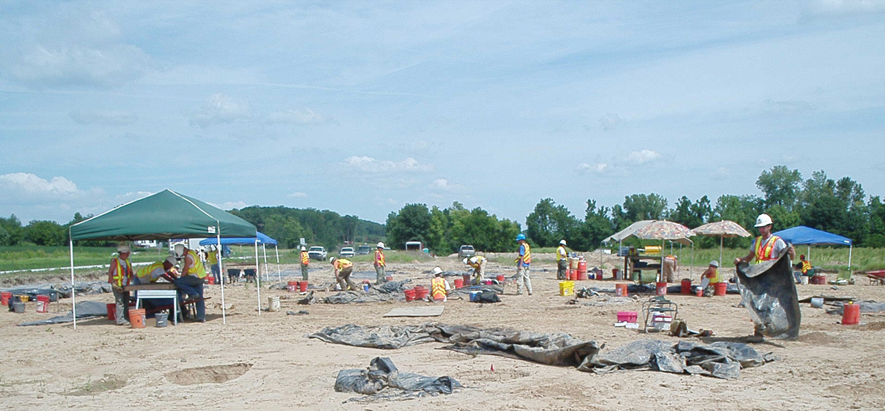 Overview of CRA crew conducting fieldwork at the site, including several tarps and tents.