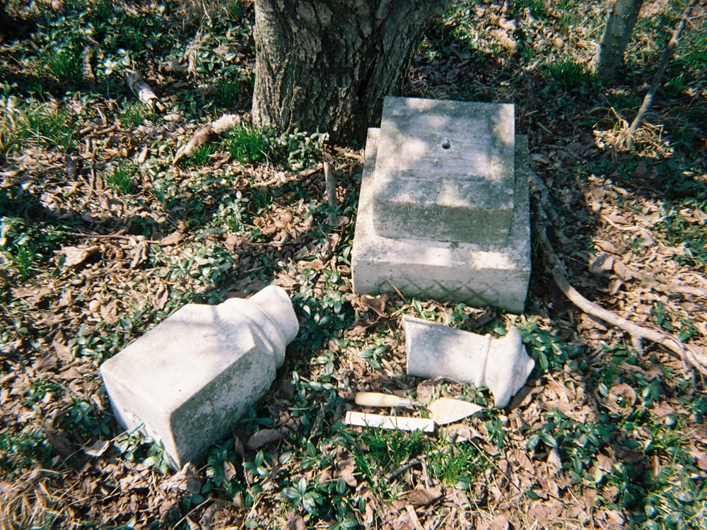 Rectangular grave marker base with two pieces of decorative extension broken on the ground.