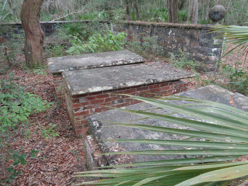 Three small brick structures capped with concrete slabs located within a stone-block fence.
