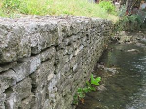 Historic stone retaining wall with river flowing at base.