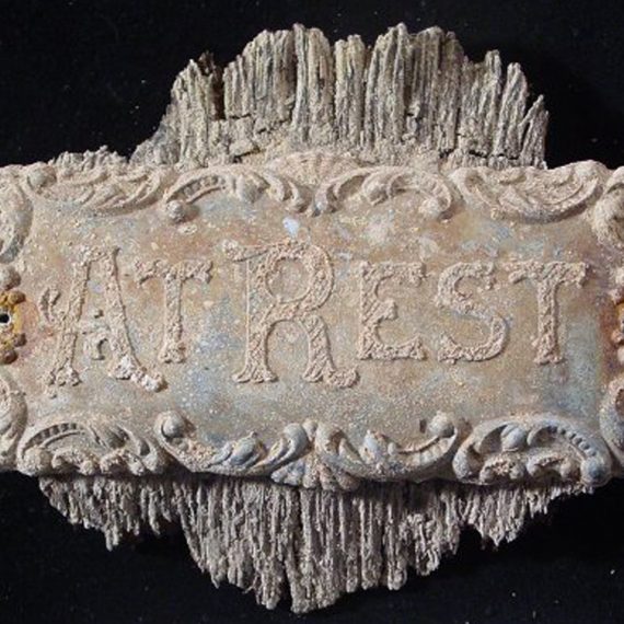 Rusted, historic plaque from casket, reading "At Rest."