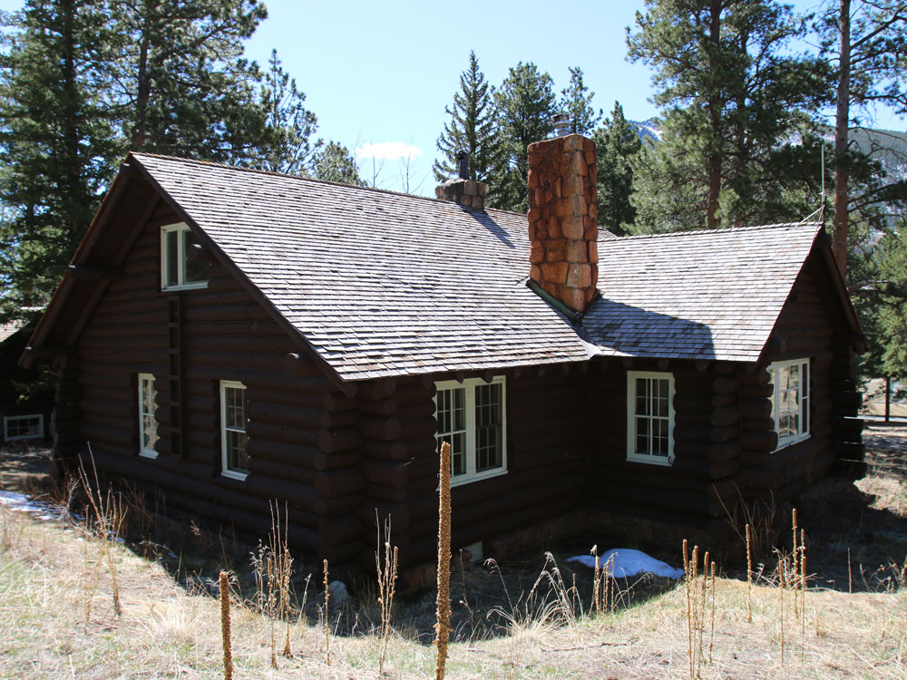Historic log cabin with shingled roof and stone chimneys.