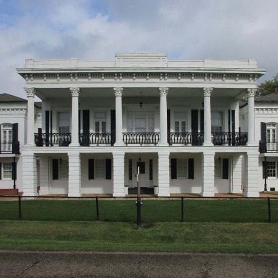 Facade of two-story historic building with sheltered porch supported by six columns.