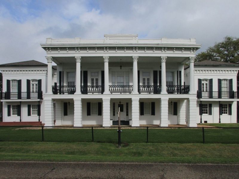 Facade of two-story historic building with sheltered porch supported by six columns.