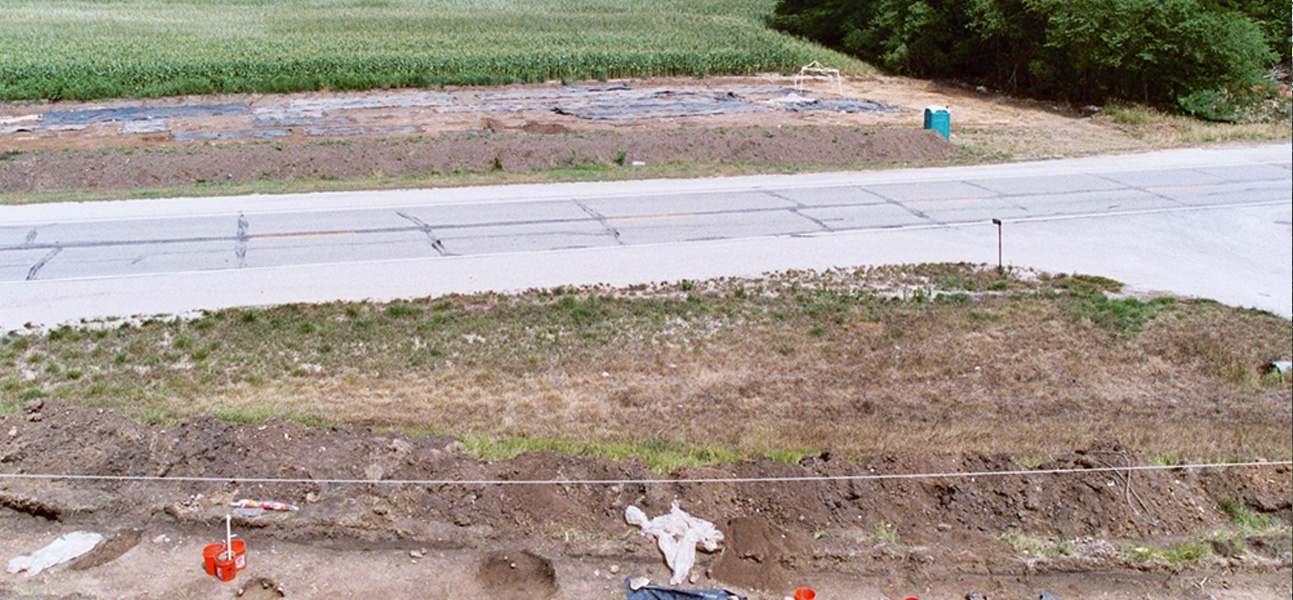 Excavated project area on either side of asphalt road.