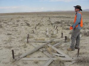 CRA crewmember standing next to remnants of a historic structure in an expansive, open dirt field.
