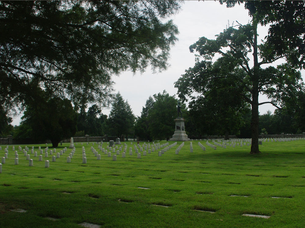 Overview of Confederate cemetery with ground-level markers in foreground, military markers in midground, and statue in background.