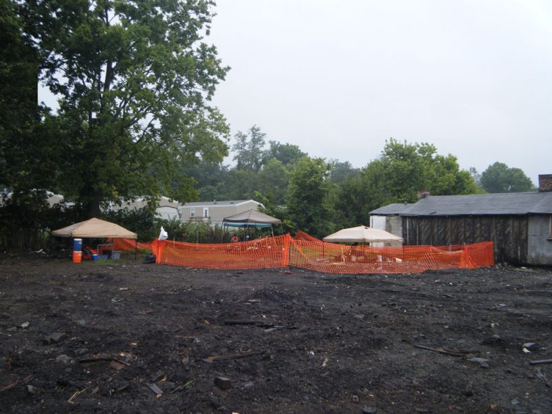 Overview of open excavation area with orange construction fence in midground.