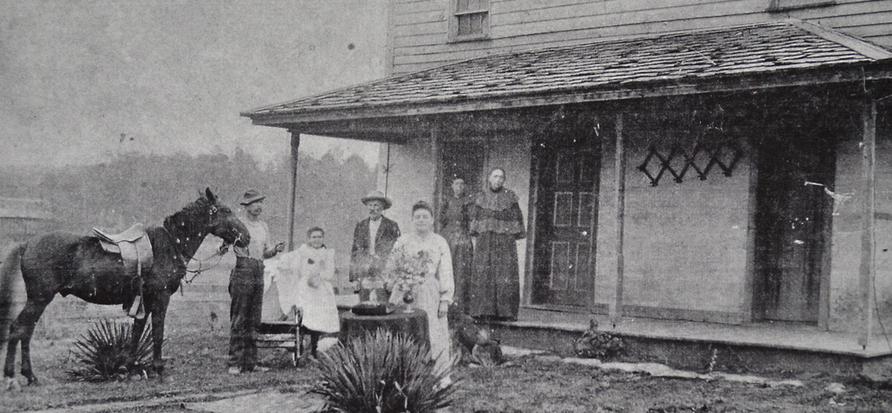 Historic black-and-white photo of Reynolds Station, featuring a group of people and a horse standing in front of the two-story building.