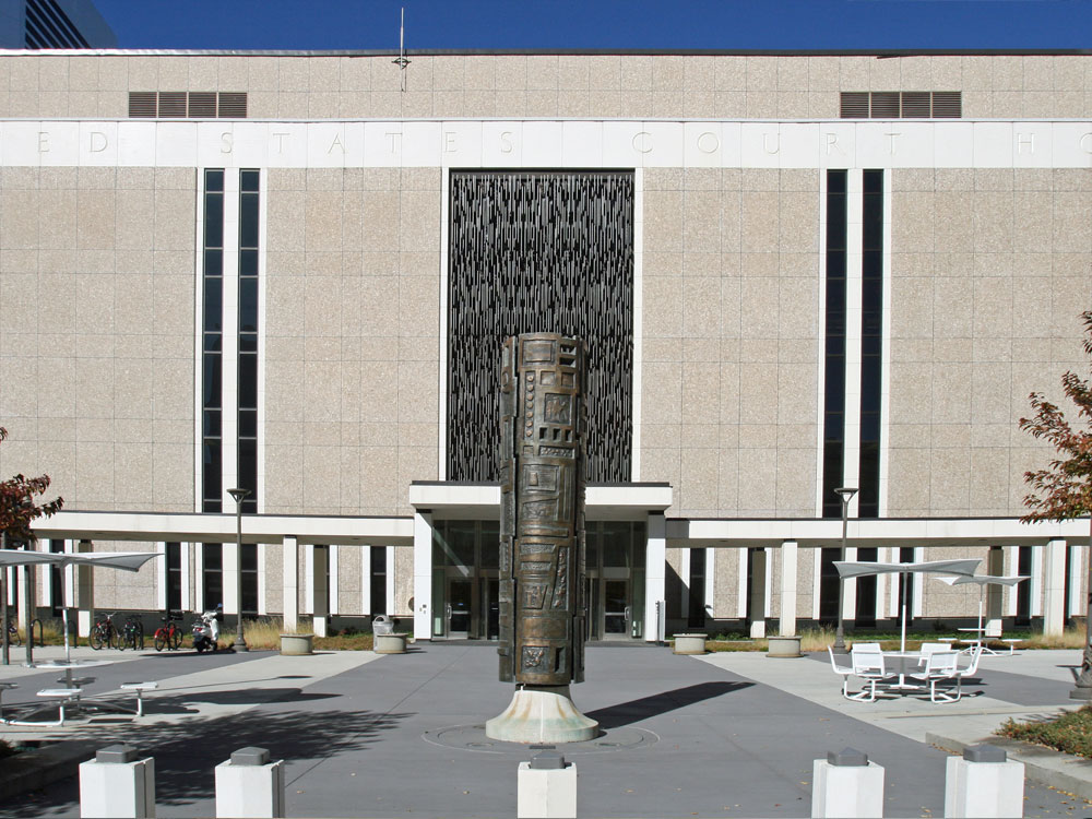 Facade of concrete courthouse building with bronze cylindrical statue in foreground.