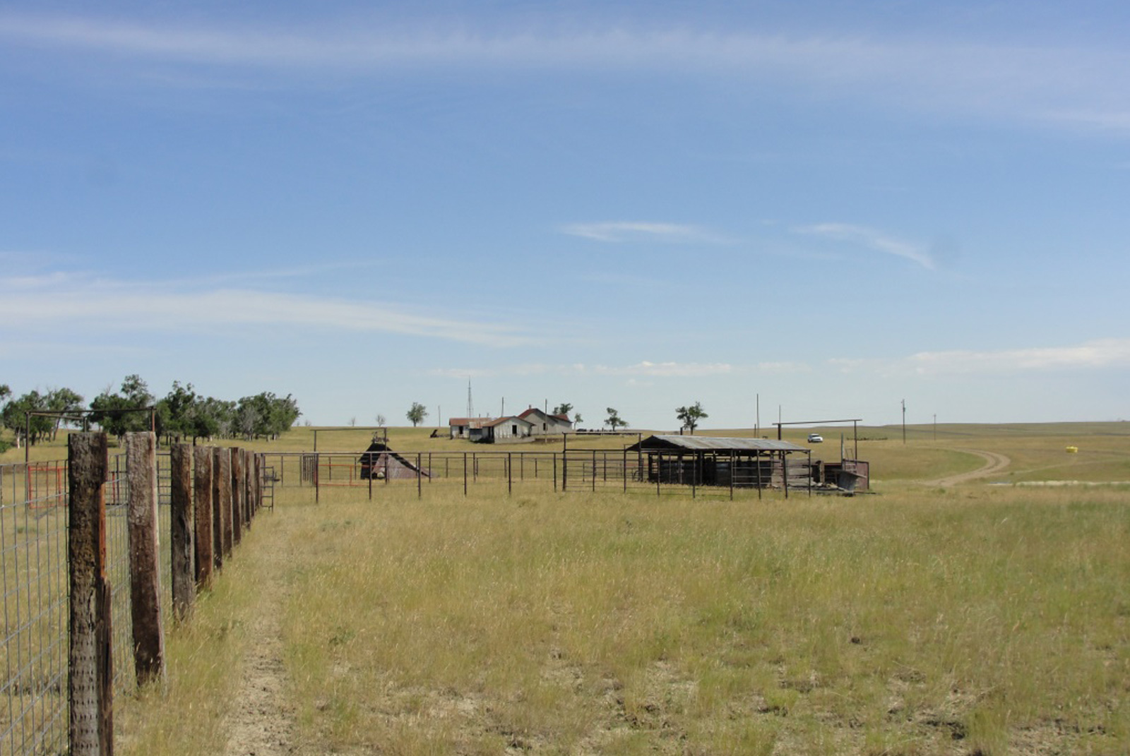 Overview of open land featuring post-and-wire fencing, outbuildings, and residence in distance.