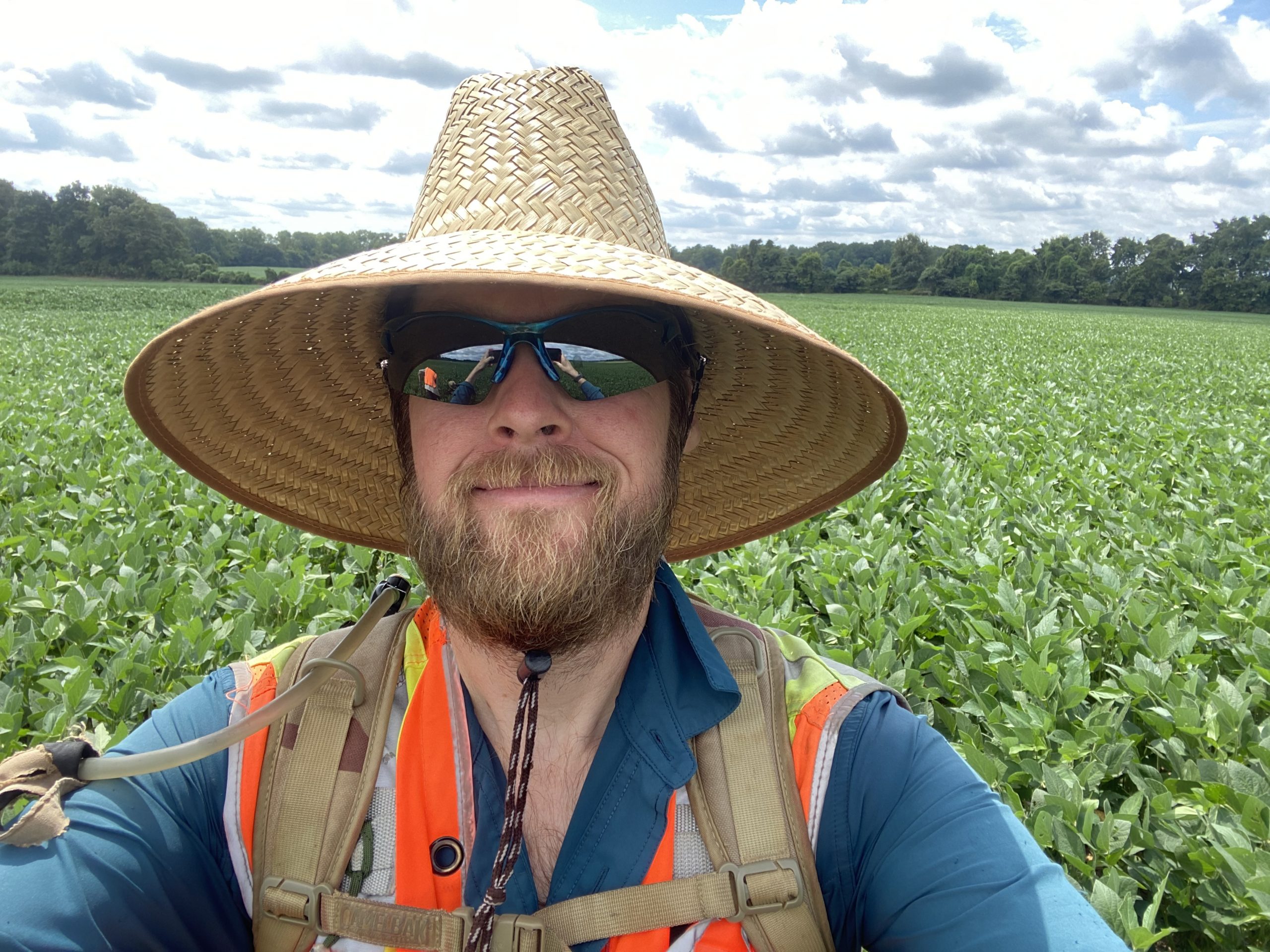Close-up of Dustin, wearing sunglasses and a sunhat, in soybean field.