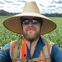 Close-up of Dustin, wearing sunglasses and a sunhat, in soybean field.