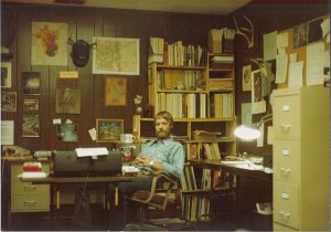 Early photo of Chuck in his first office, featuring many photos and documents hanging on the wall.