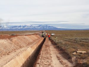 Crewmembers digging deep trench with mountains in background.