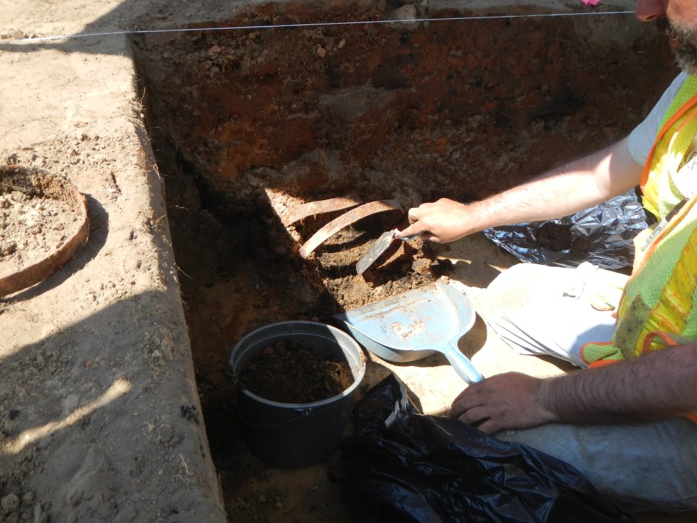 Crewmember uncovering rusted metal artifacts from excavation.