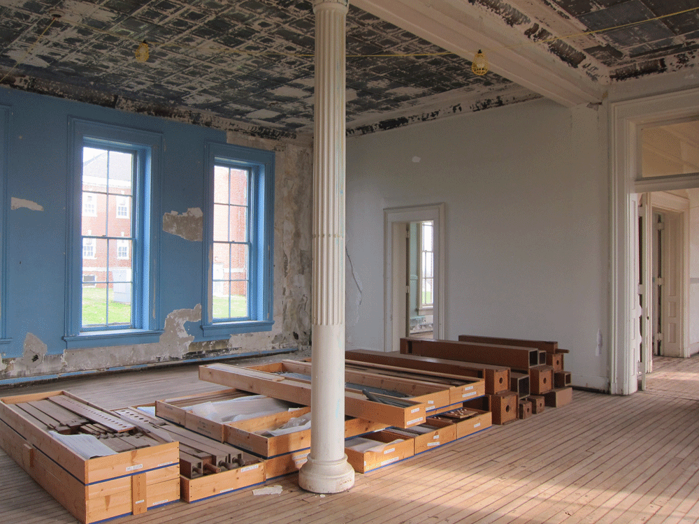 Interior of historic building with support column and wooden materials stacked at center.