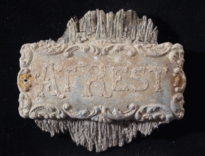 Rusted, historic plaque from casket, reading, "At Rest."