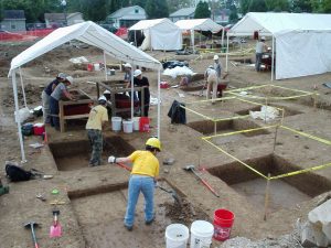 CRA crew conducting fieldwork in open excavated area, including many tents and large test pits.