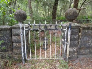 Metal entrance gate for stone-block fence; piers flanking the gate are topped by stone spheres.