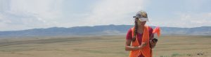 CRA crewmember standing in vast, open plain with mountains in distant background.