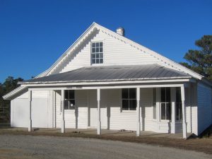 Facade of side-gable building with white siding and metal-panel porch overhang.
