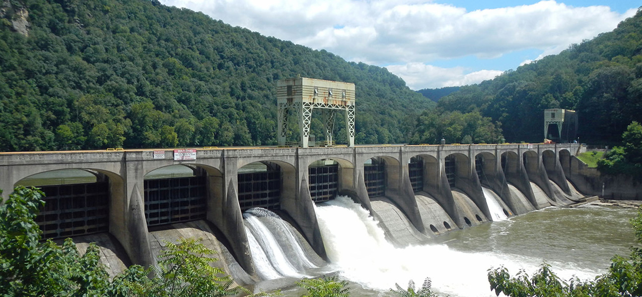 Overview of Hawks Nest Dam, an immense concrete structure with water gushing from its openings.