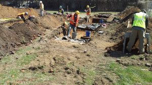 Crewmembers conducting fieldwork in shallow excavation area.