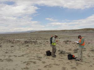 CRA crewmembers standing in expansive dirt field with mountains in distance.