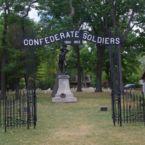 Metal entrance gate to Confederate cemetery with overhead sign reading "Confederate Soldiers 1861 1912" and bronze statue in midground.