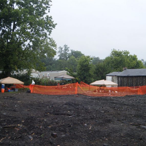 Overview of open excavation area with orange construction fence in midground.