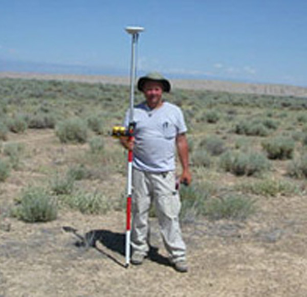 Randy standing in open field, holding survey equipment.