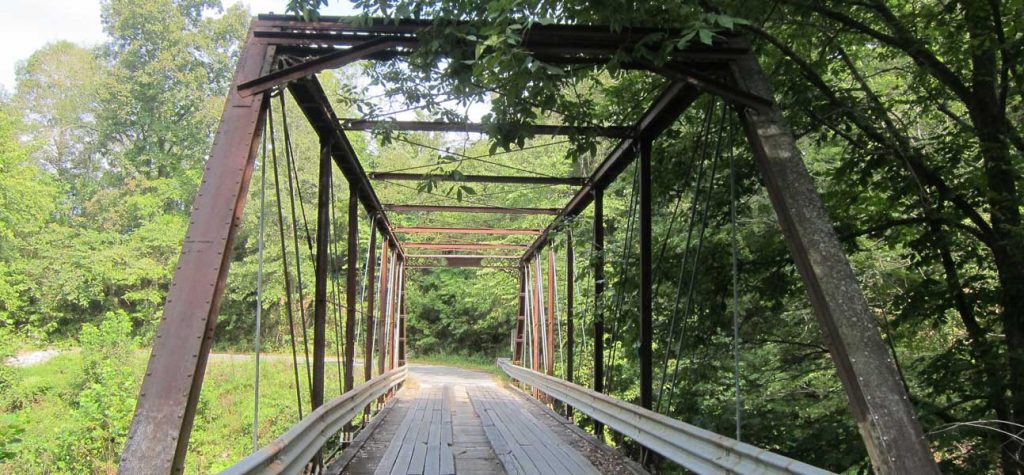 Historic bridge, constructed of metal framing and guardrails and wooden floor, shown from road entrance.